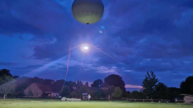A large balloon floats above a green meadow. A bright light shines from the balloon, illuminating the meadow.